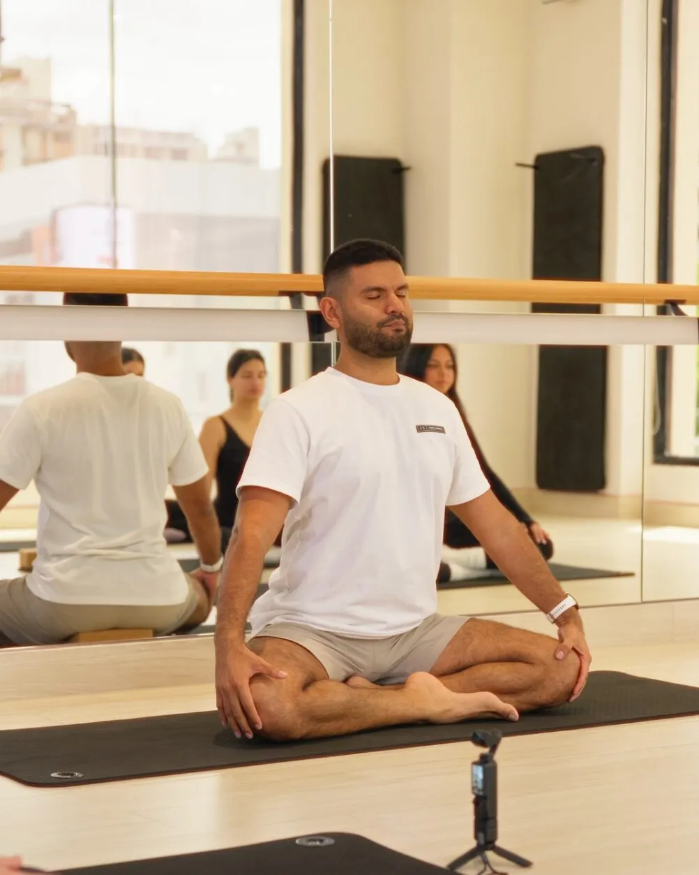 Un instructor sentado con las piernas cruzadas sobre la colchoneta, junto a la barra.
